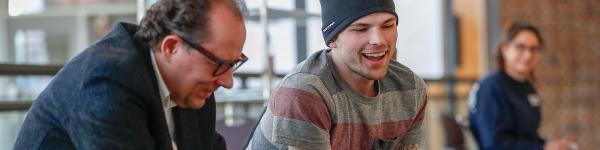 Male student in beanie hat smiling and talking with instructor.
