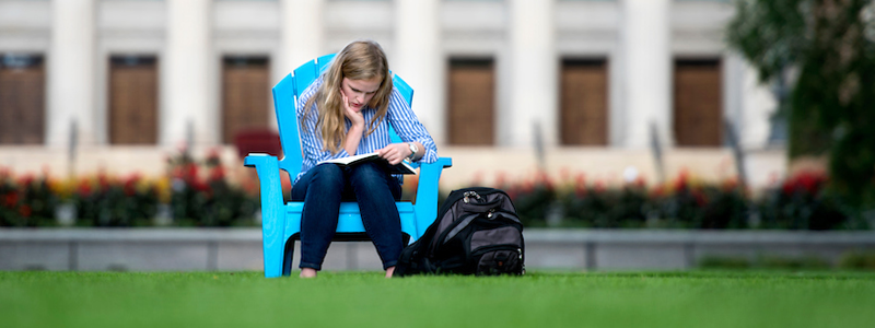Student sitting in chair on the mall lawn studying.