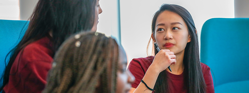 PHOTO: female presenting student looks pensively at another student, chin resting on hand.